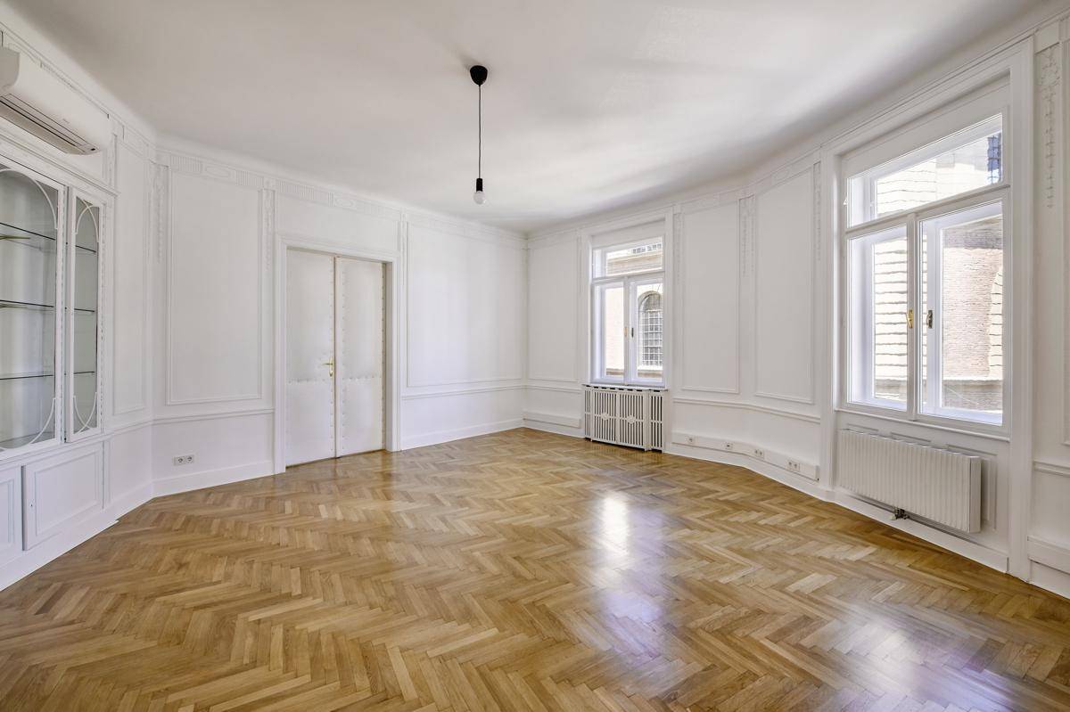 Elegantes Wohnzimmer mit Fischgrätparkett, hohen Fenstern und integriertem Wandschrank.