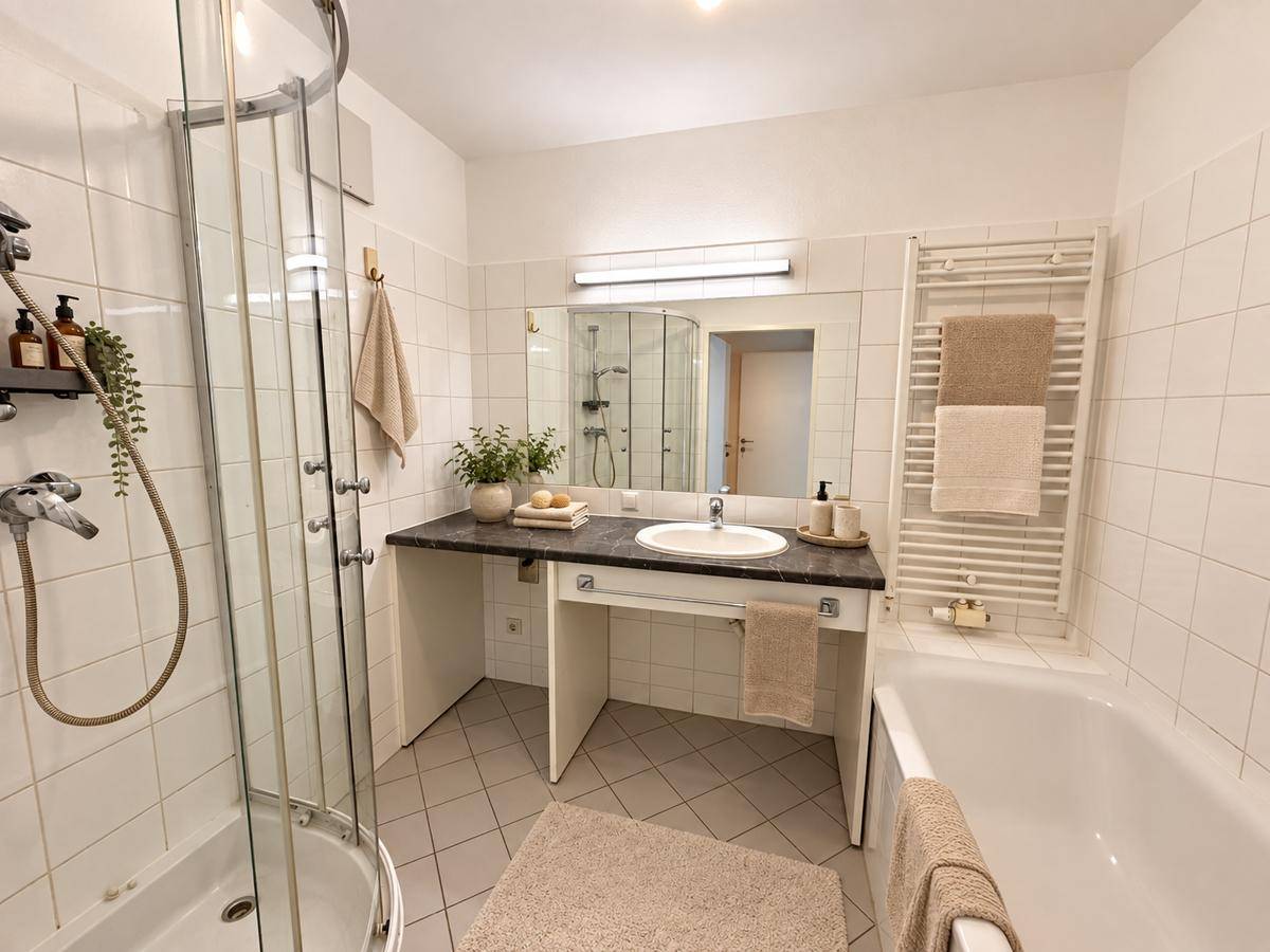 Helles Badezimmer mit Badewanne, Dusche, Einzelwaschbecken und beheiztem Handtuchhalter.