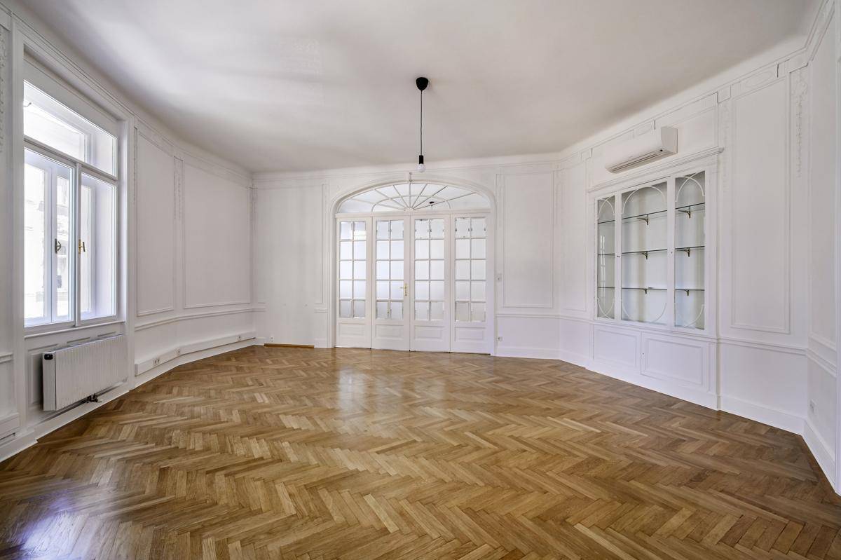Geräumiges Wohnzimmer mit Fischgrätparkett, hohen Fenstern und einem eleganten Wandschrank.