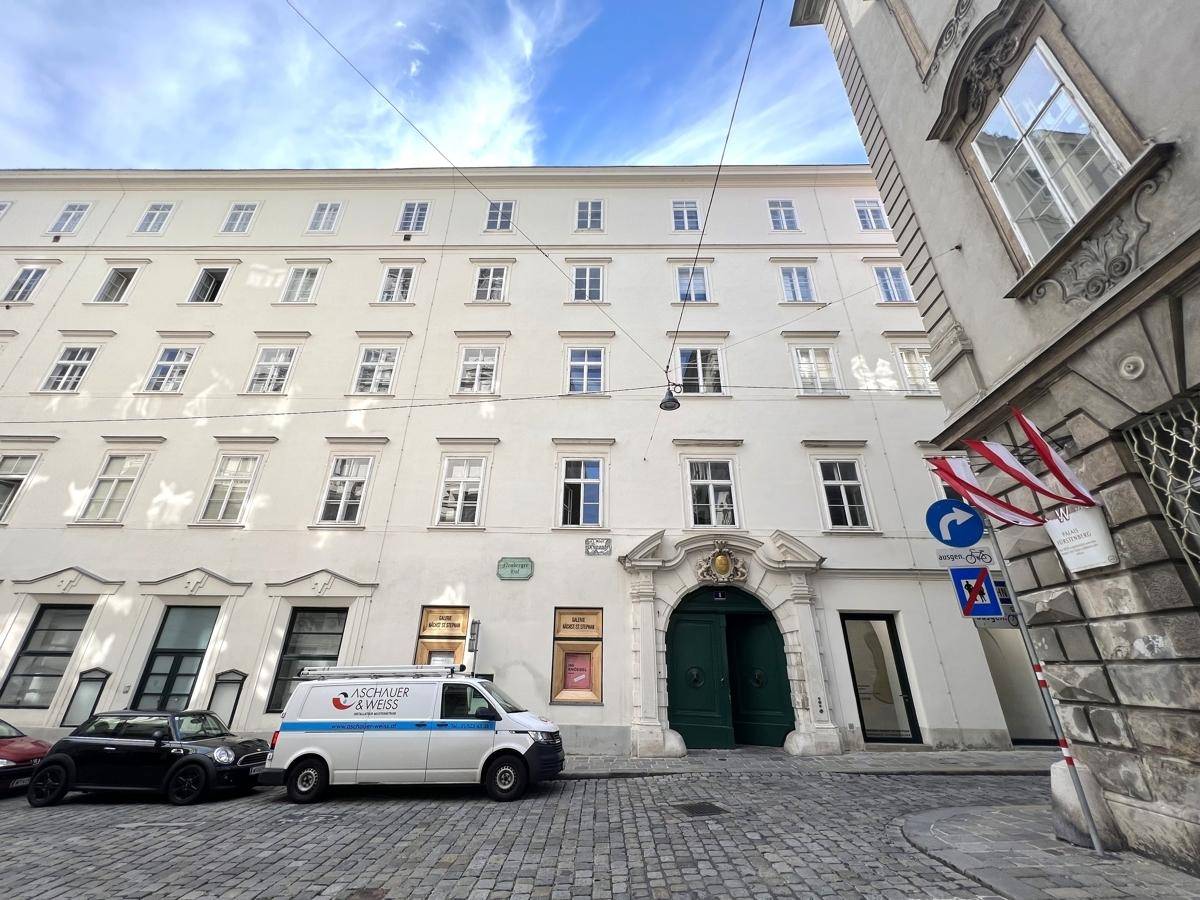 Historische Fassade eines Gebäudes in der Stadt mit gepflasterter Straße und parkenden Autos.