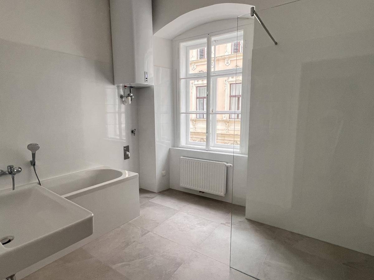 Helles Badezimmer mit Badewanne, Einzelwaschbecken und Fenster.