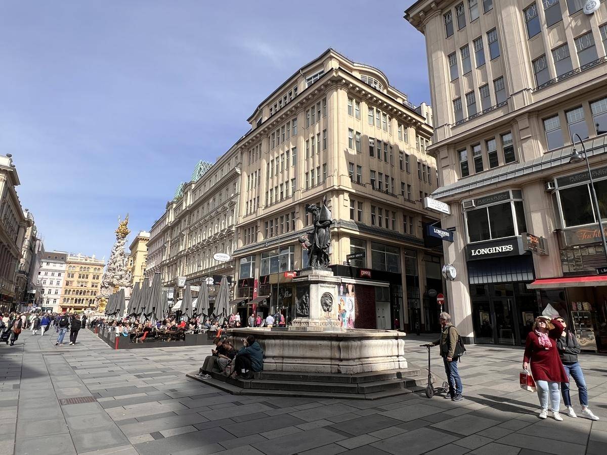Eine belebte Stadtstraße mit einem prächtigen Gebäude, einem Brunnen und vielen Menschen im Freien.