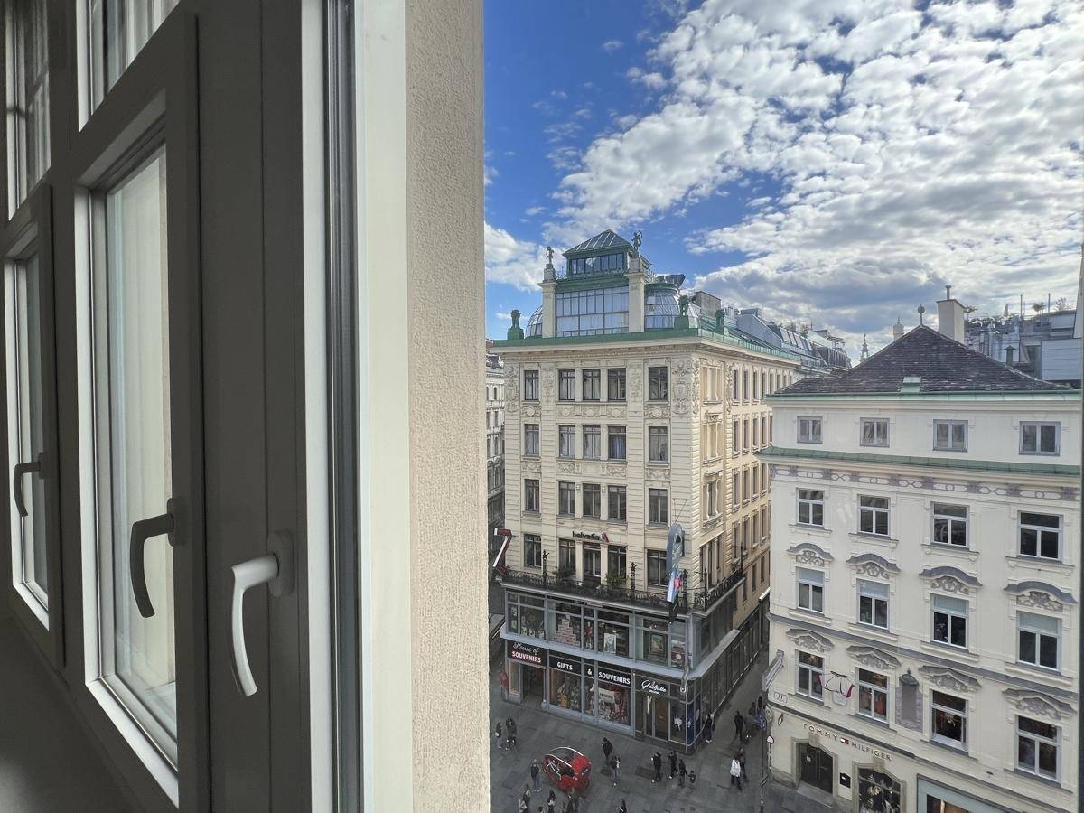 Blick aus dem Fenster auf eine belebte Stadtstraße mit historischen Gebäuden und blauem Himmel.