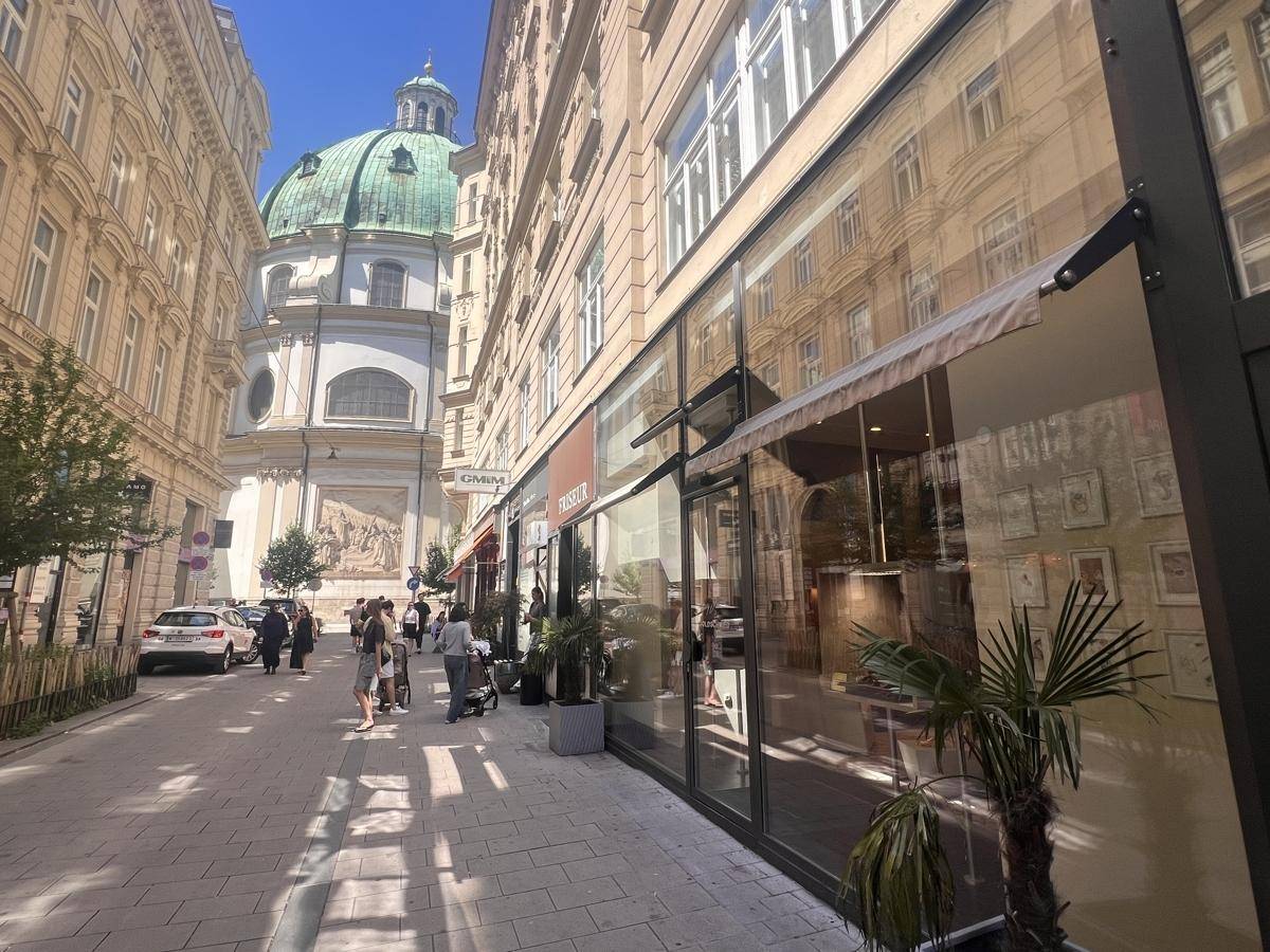 Eine belebte Straße in Wien mit einem modernen Geschäftsgebäude und einer historischen Kirche im Hintergrund.