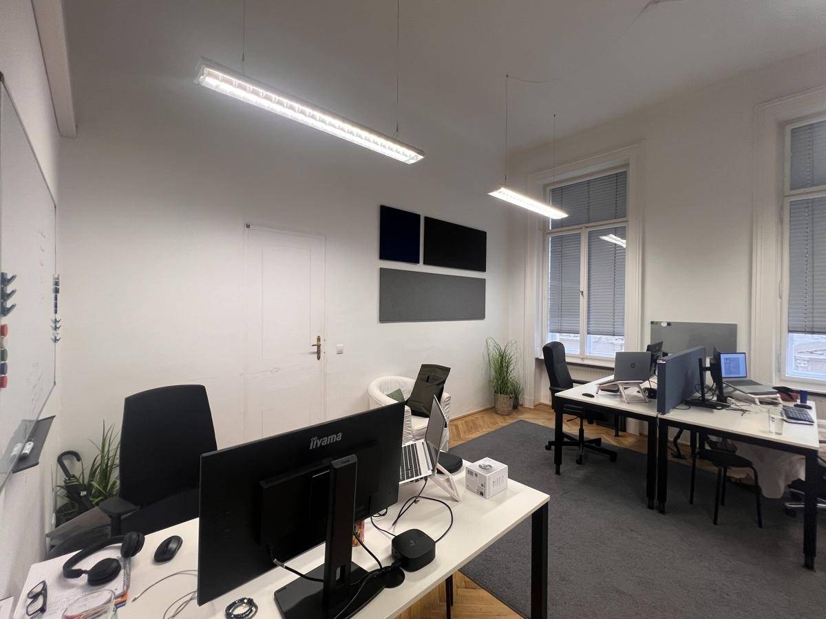 Offener Bürobereich mit mehreren Arbeitsplätzen, großen Fenstern und Teppichboden, funktional gestaltet.