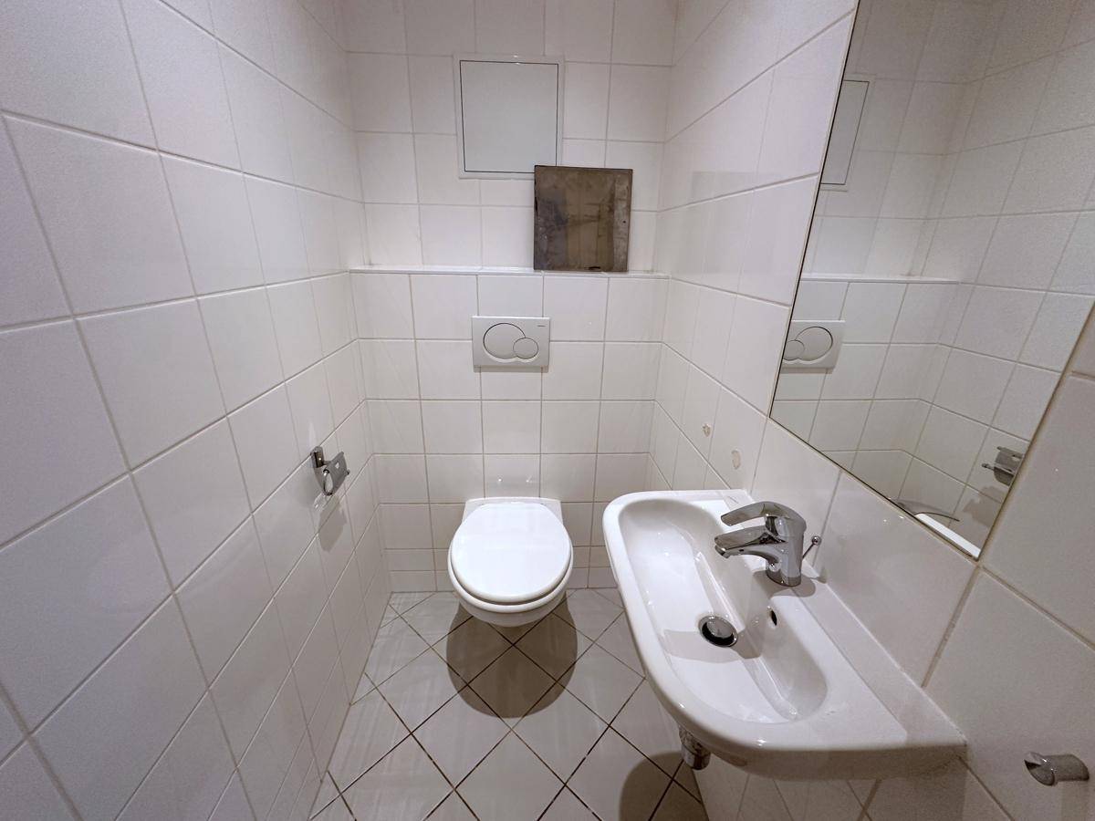 Kleines, gefliestes Gäste-WC mit Toilette, Waschbecken und Spiegel.