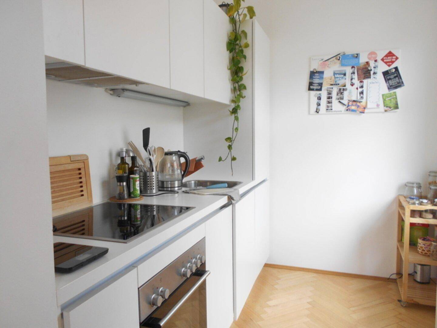 Moderne Küchenzeile mit weißen Schränken, Induktionskochfeld und Backofen, funktional und hell.