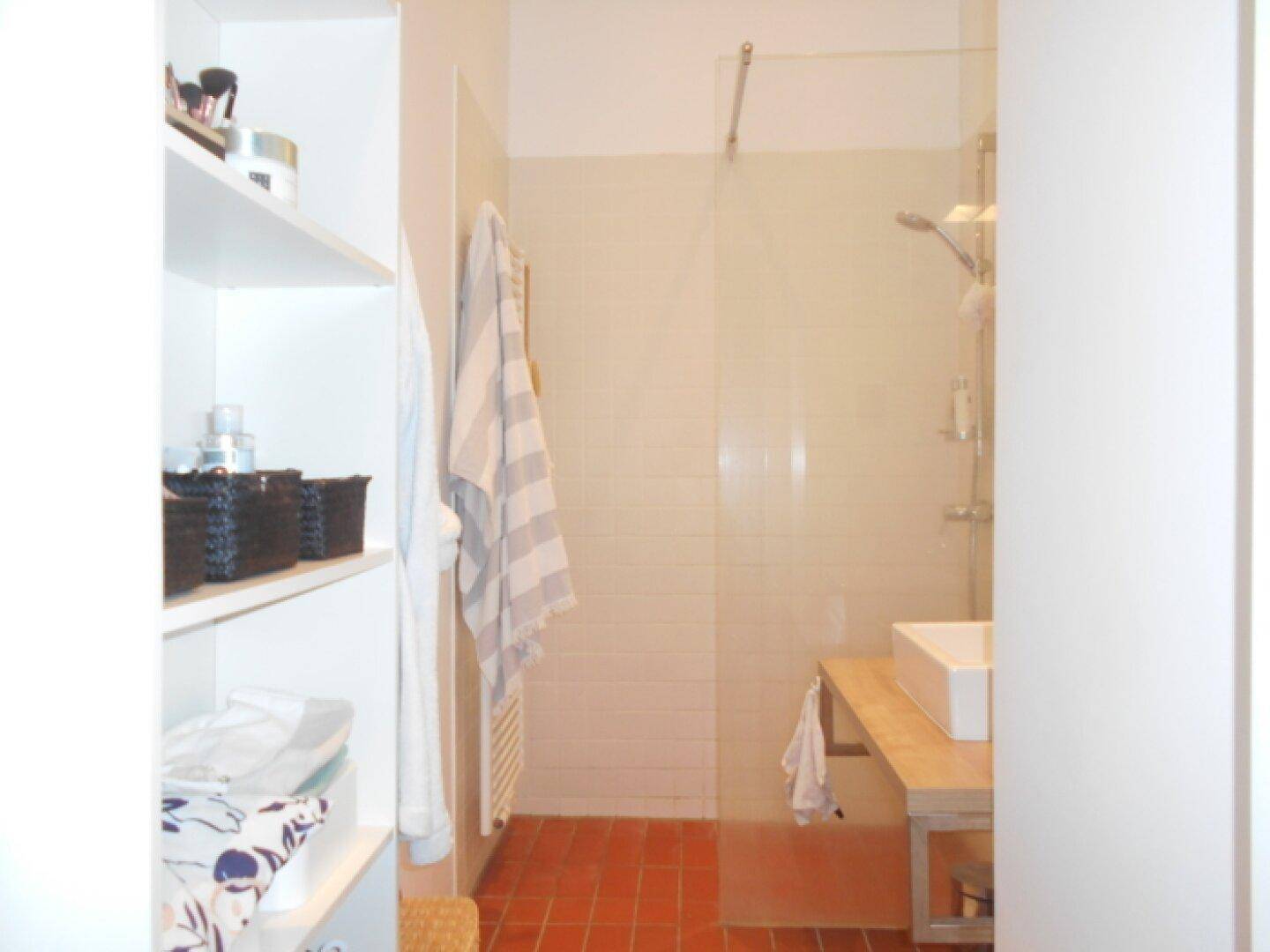 Badezimmer mit Duschbereich, modernem Waschbecken auf Holzplatte und praktischen Regalen.