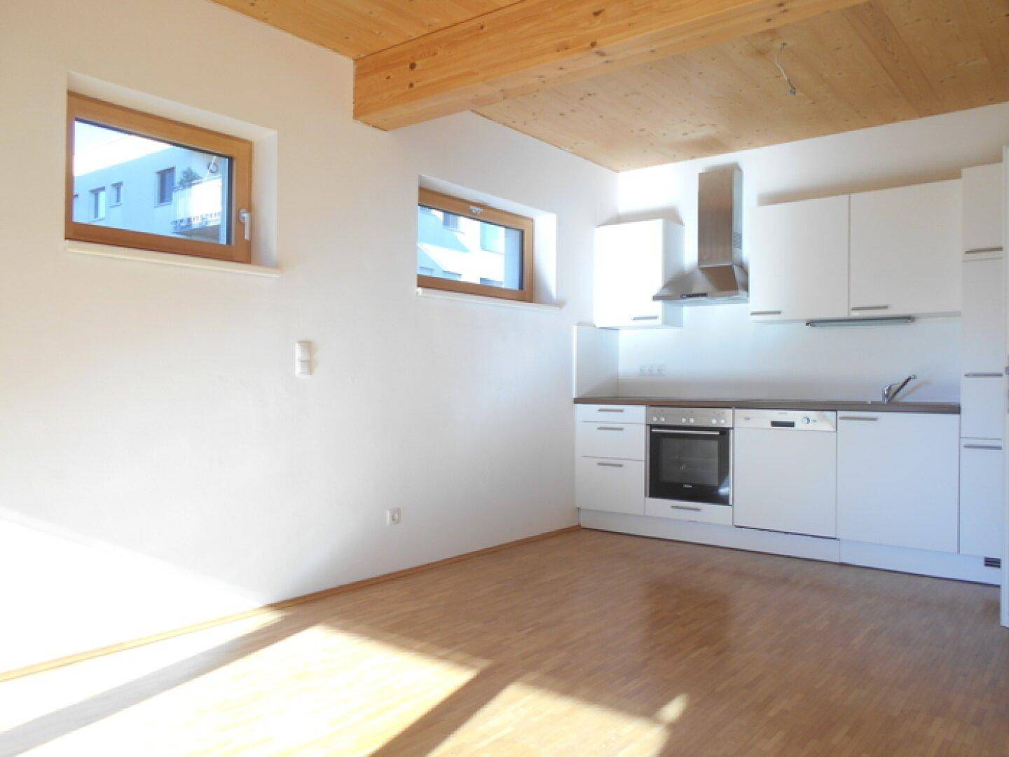 Helle Küche mit weißen Schränken, Holzdecke und zwei Fenstern, die viel Tageslicht hereinlassen.