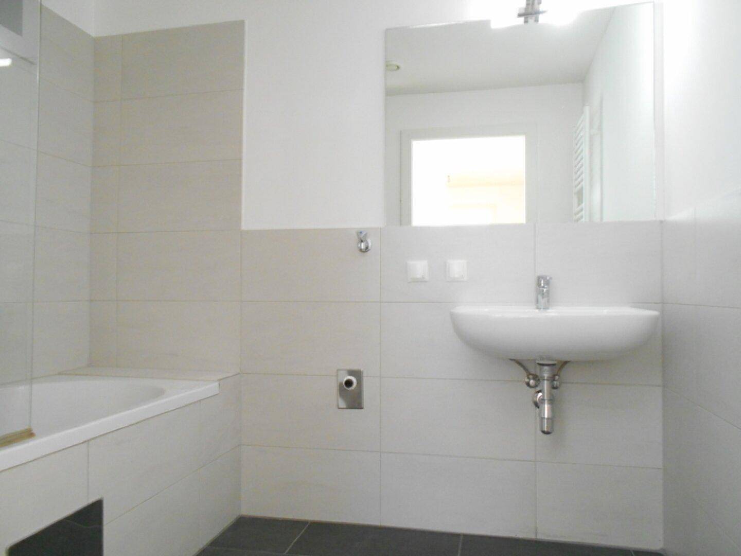Modernes Badezimmer mit Badewanne, Waschbecken und hellen Fliesen, ausgestattet mit einem Spiegel.