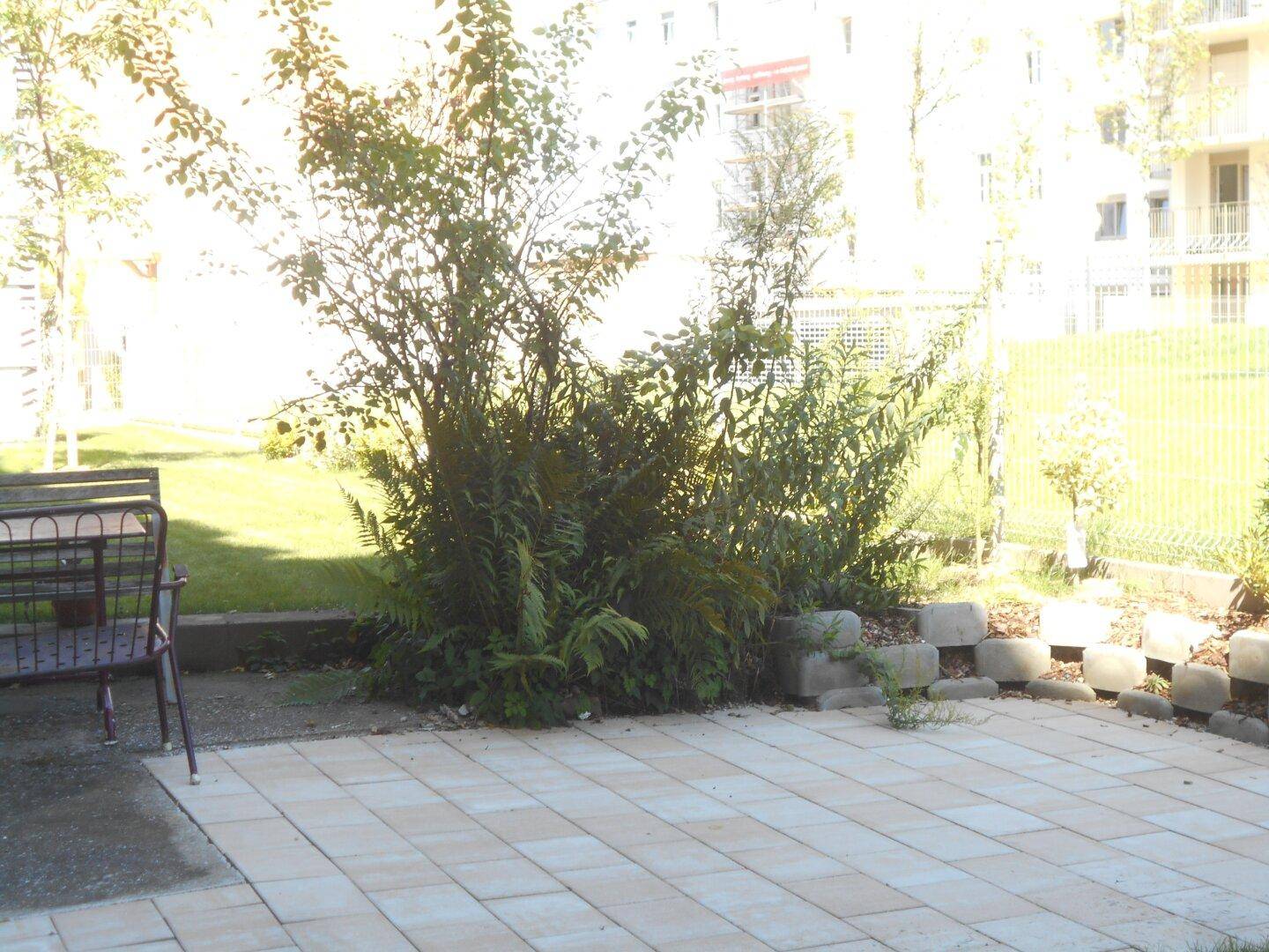 Gepflasterte Terrasse mit Pflanzen und einem Tisch, angrenzend an eine grüne Rasenfläche.