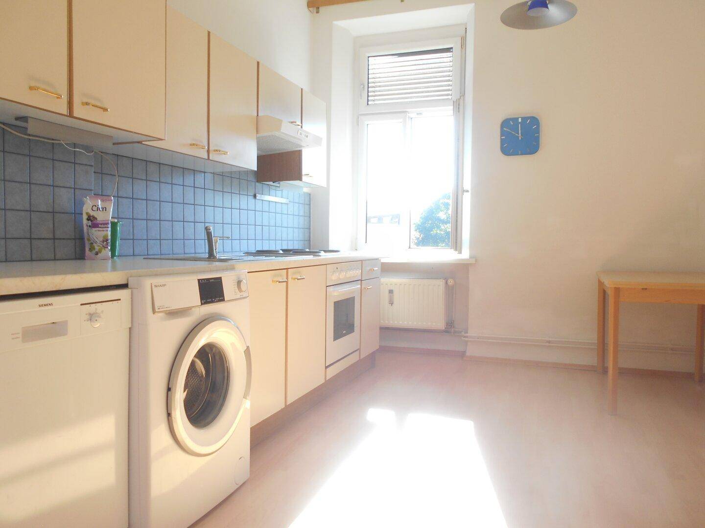 Funktionale Küche mit hellen Schränken, Spülmaschine, Waschmaschine und einem Fenster für Tageslicht.