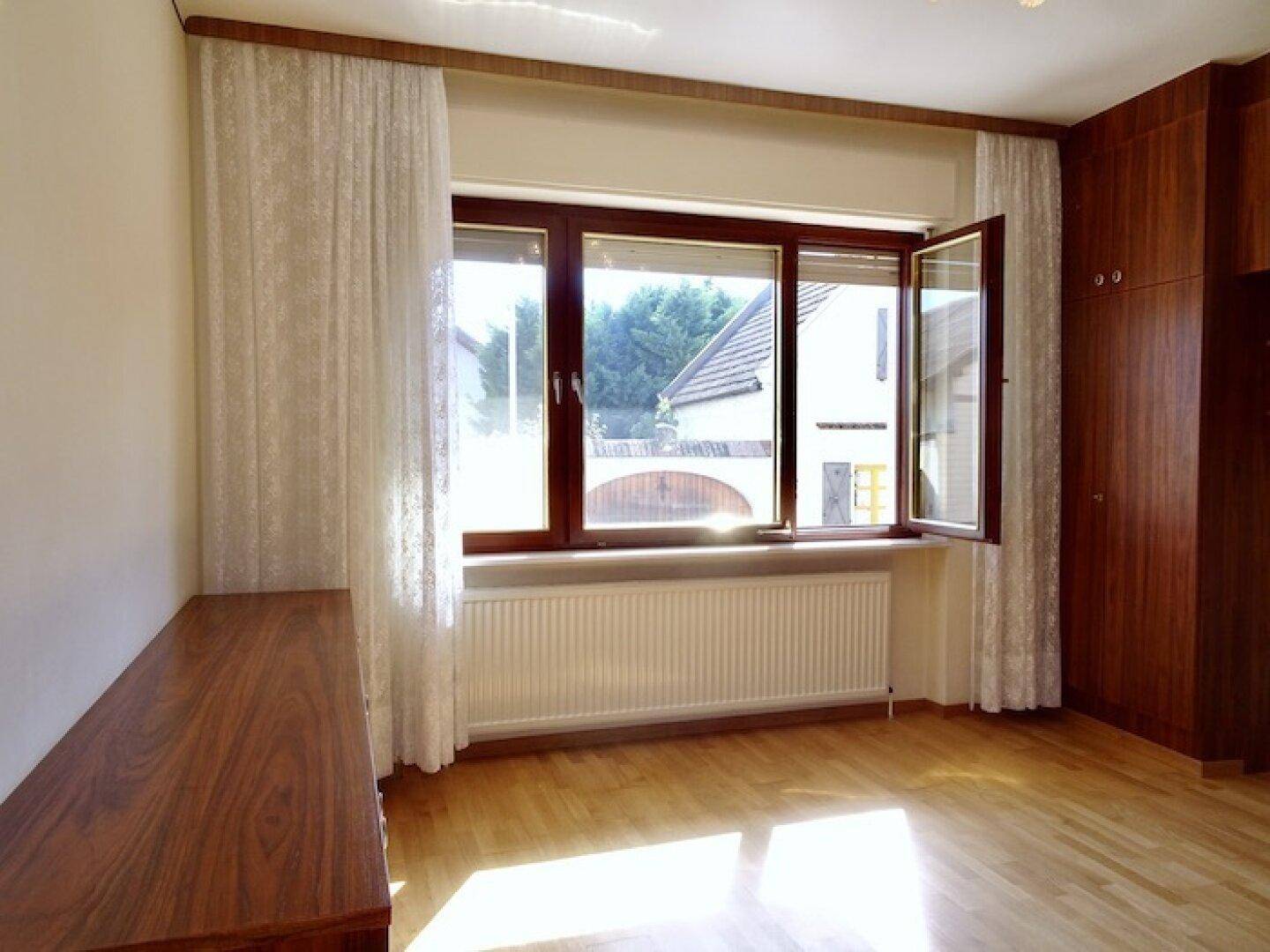 Schlafzimmer mit Parkettboden, großen Fenstern und einem Einbauschrank aus dunklem Holz.