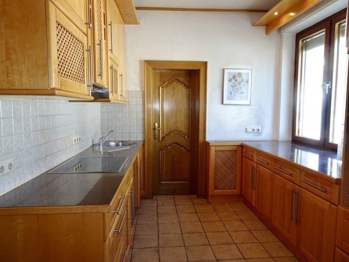 Traditionelle Küche mit Holzschränken, Fliesenboden und dunklen Arbeitsplatten.