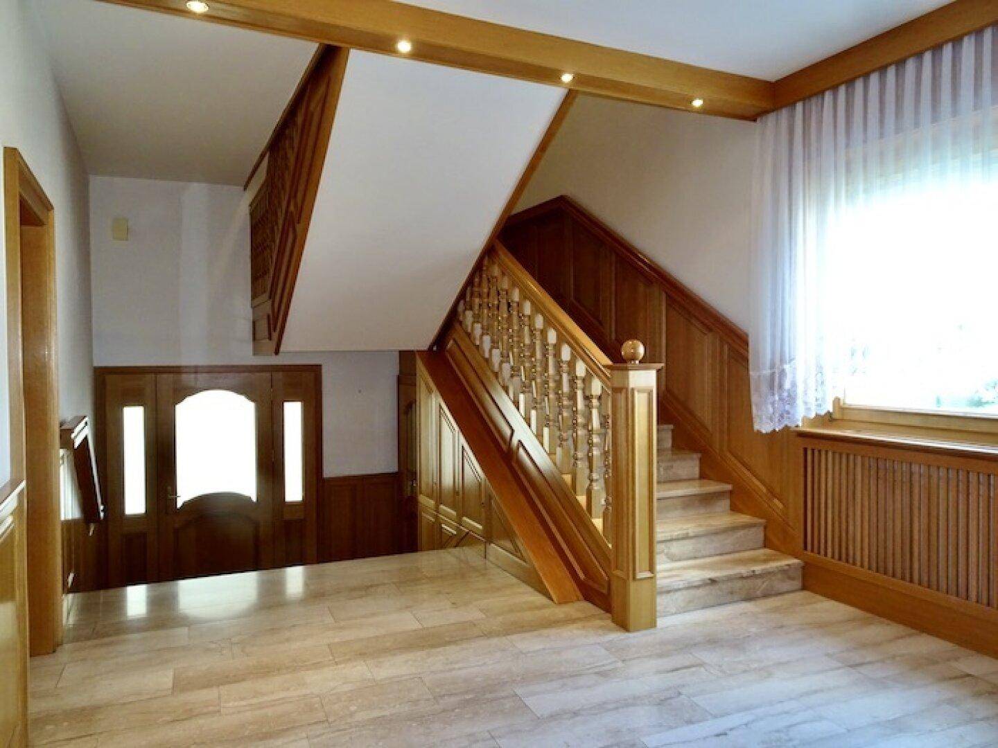 Geräumiger Eingangsbereich mit Holztreppe, Marmorboden und einer großen Holztür.