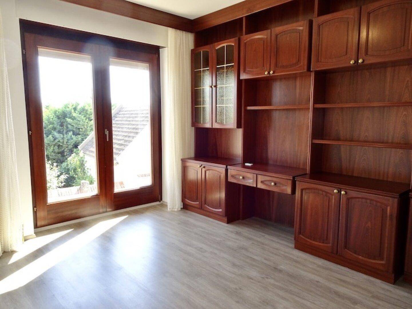 Zimmer mit Einbauschränken aus dunklem Holz, Laminatboden und Zugang zu einem Balkon.