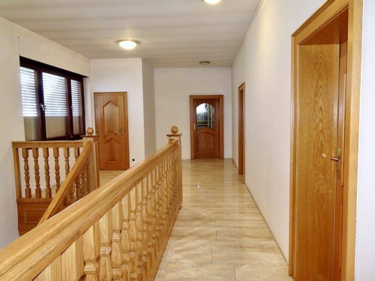 Heller Flur im Obergeschoss mit Holzgeländer, Steinboden und mehreren Türen.