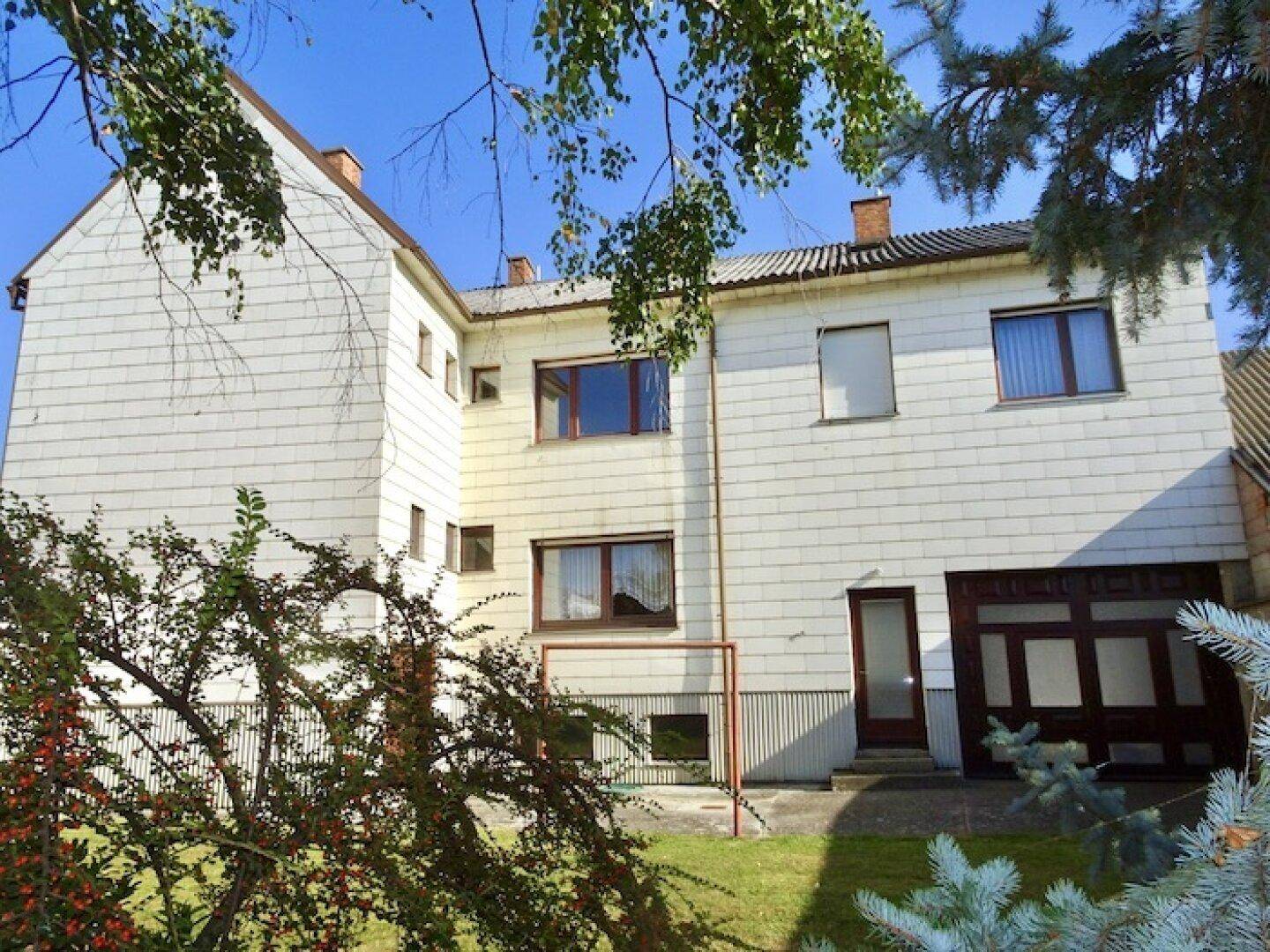 Rückansicht des Gebäudes mit weißer Fassade, Fenstern und einem gepflegten Gartenbereich.