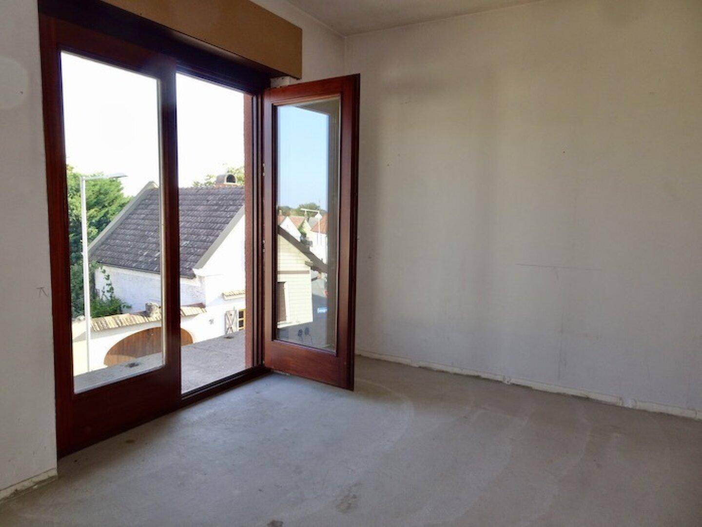 Leerer Raum mit Betonboden und Zugang zu einem Balkon, bereit für die Gestaltung.