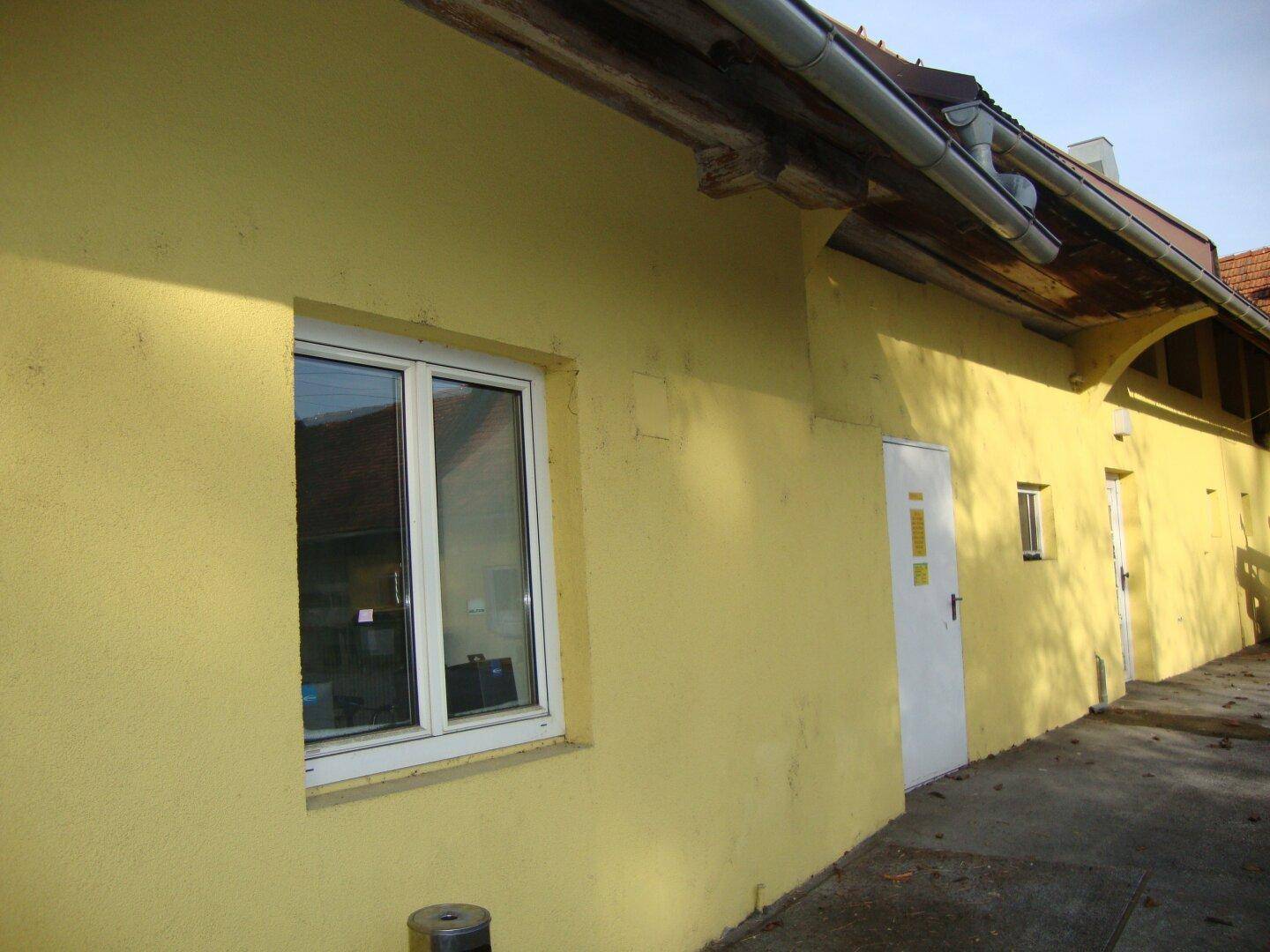 Längsseite des gelben Gebäudes mit modernen Fenstern, zwei Türen und einem Dachrinnensystem.