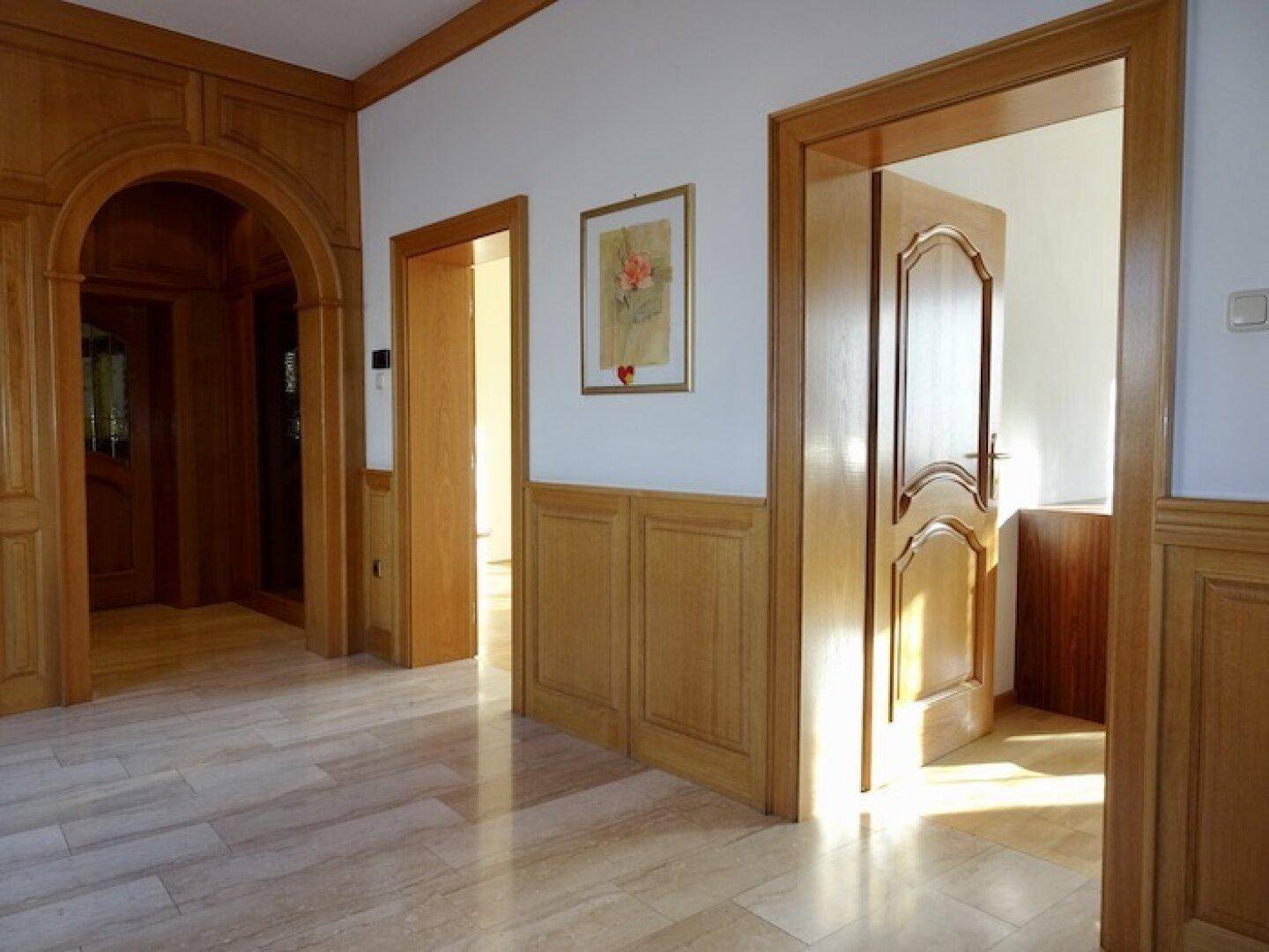 Heller Flur mit Holztüren, Holzvertäfelung und einem Bogen, der zu weiteren Räumen führt.