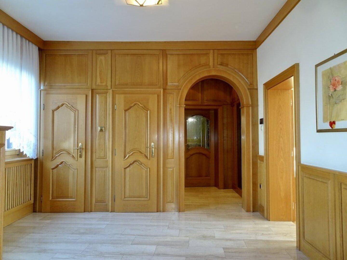 Geräumiger Flur mit heller Holzvertäfelung, Holztüren und hellem Fliesenboden, der zu weiteren Räumen führt.