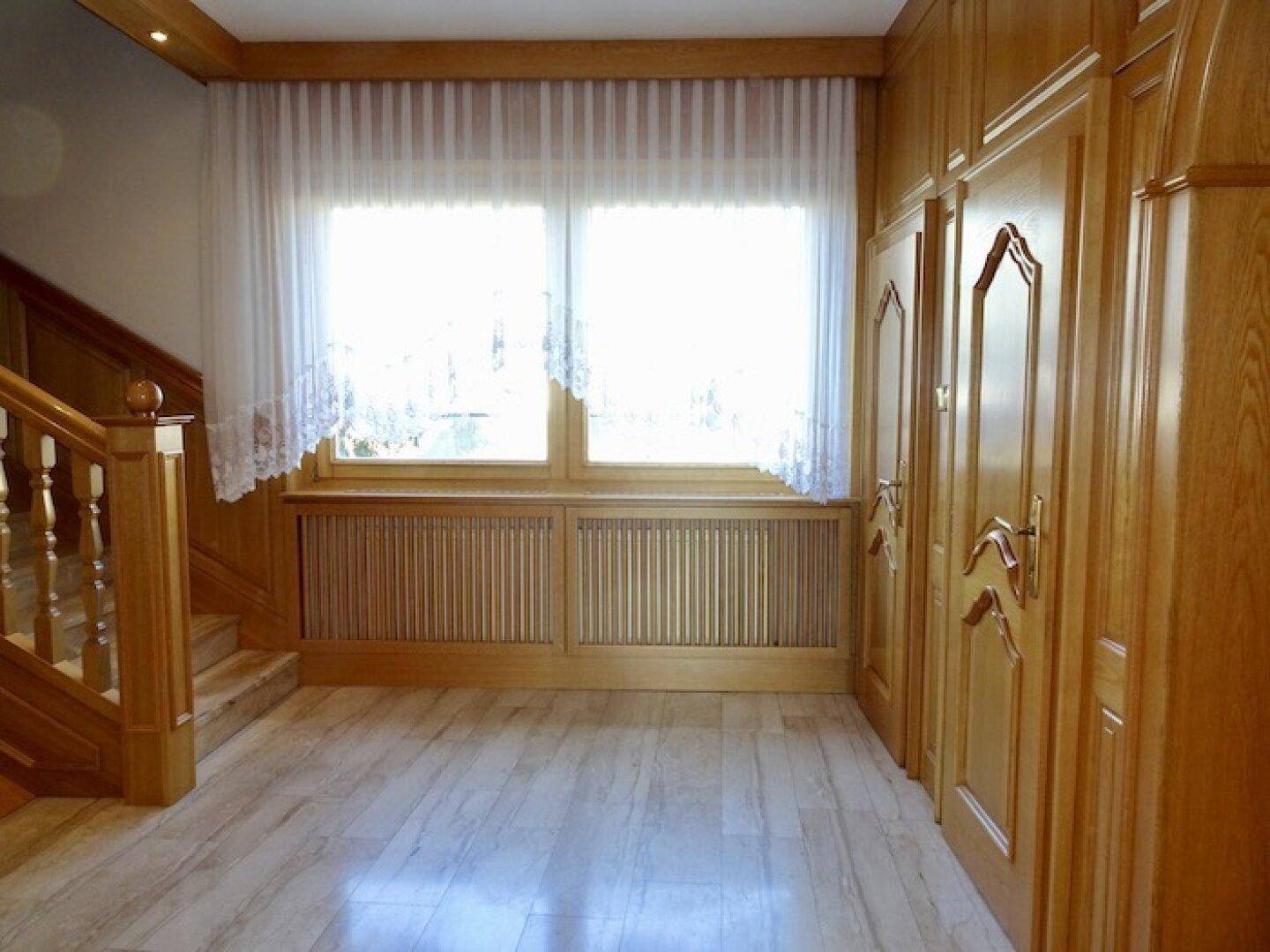 Geräumiger Eingangsbereich mit Holztreppe, Holzvertäfelung und hellem Fliesenboden, gut beleuchtet.