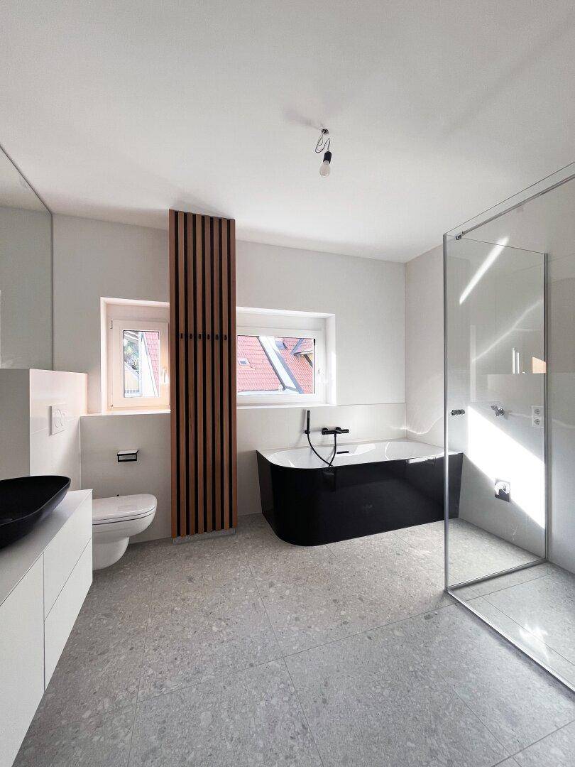 Elegantes Badezimmer mit freistehender schwarzer Badewanne, begehbarer Dusche und Fenster.