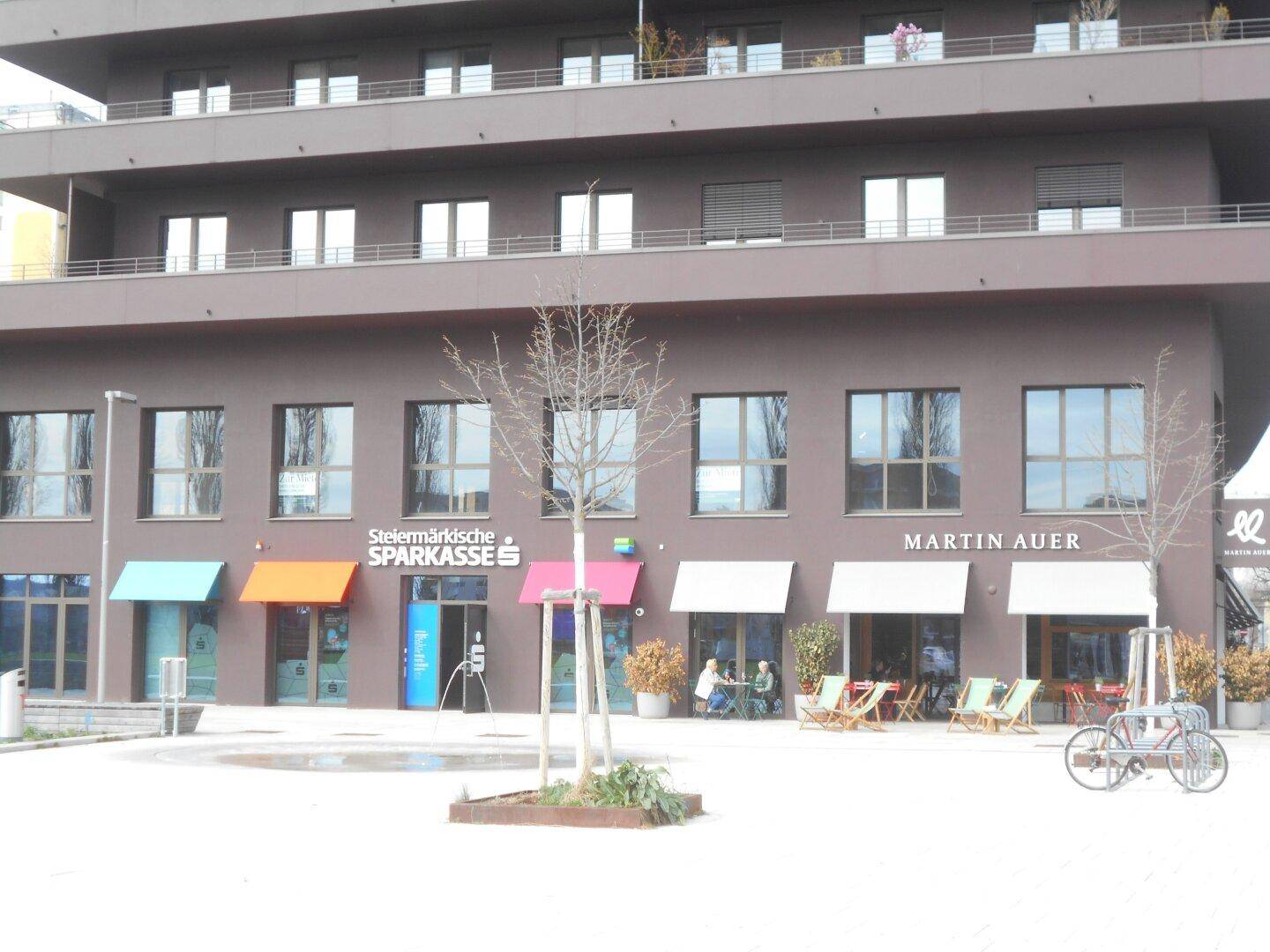 Moderne Geschäftsfassade im Erdgeschoss eines Gebäudes mit verschiedenen Läden und einem Café.