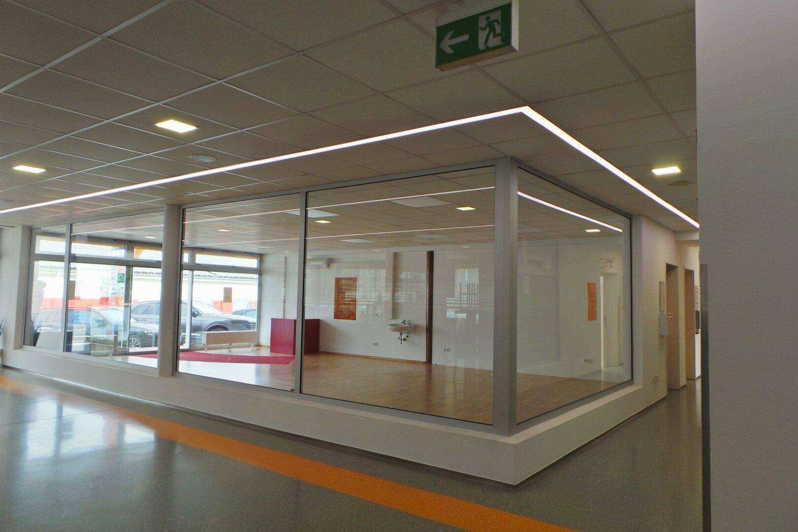 Heller Gewerberaum mit großen Glaswänden, Holzboden und moderner Deckenbeleuchtung.