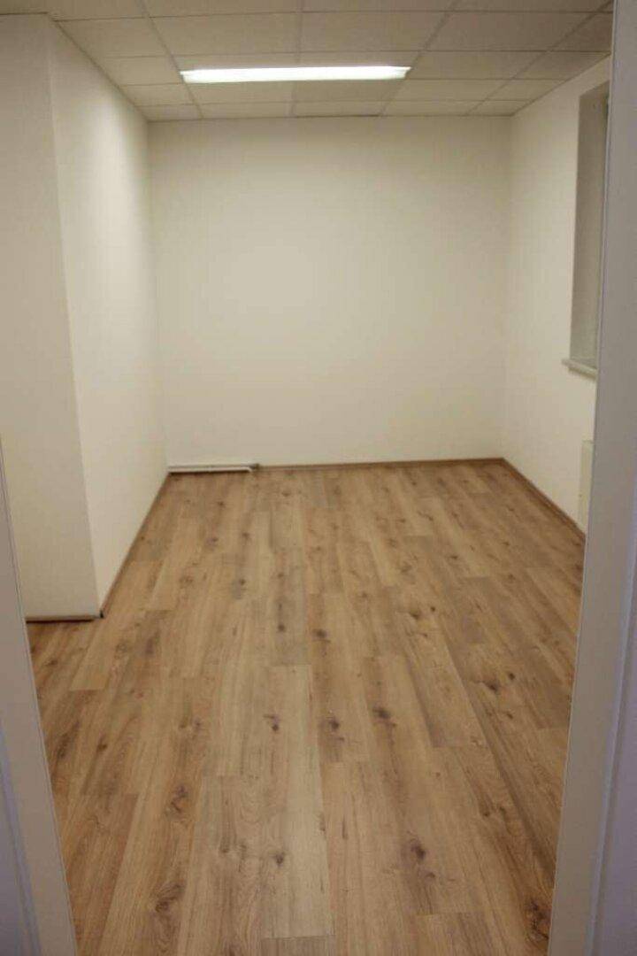 Leerer Büroraum mit hellem Holzboden, weißen Wänden und Deckenbeleuchtung.
