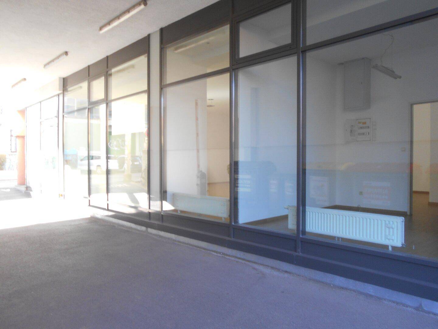 Lange Glasfront eines modernen Geschäftsgebäudes mit überdachtem Gehweg und Heizkörpern hinter den Fenstern.
