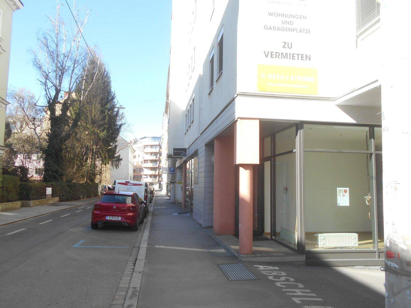 Straßenansicht eines modernen Gebäudes mit Gewerbeflächen im Erdgeschoss und Wohnungen darüber, umgeben von Bäumen.