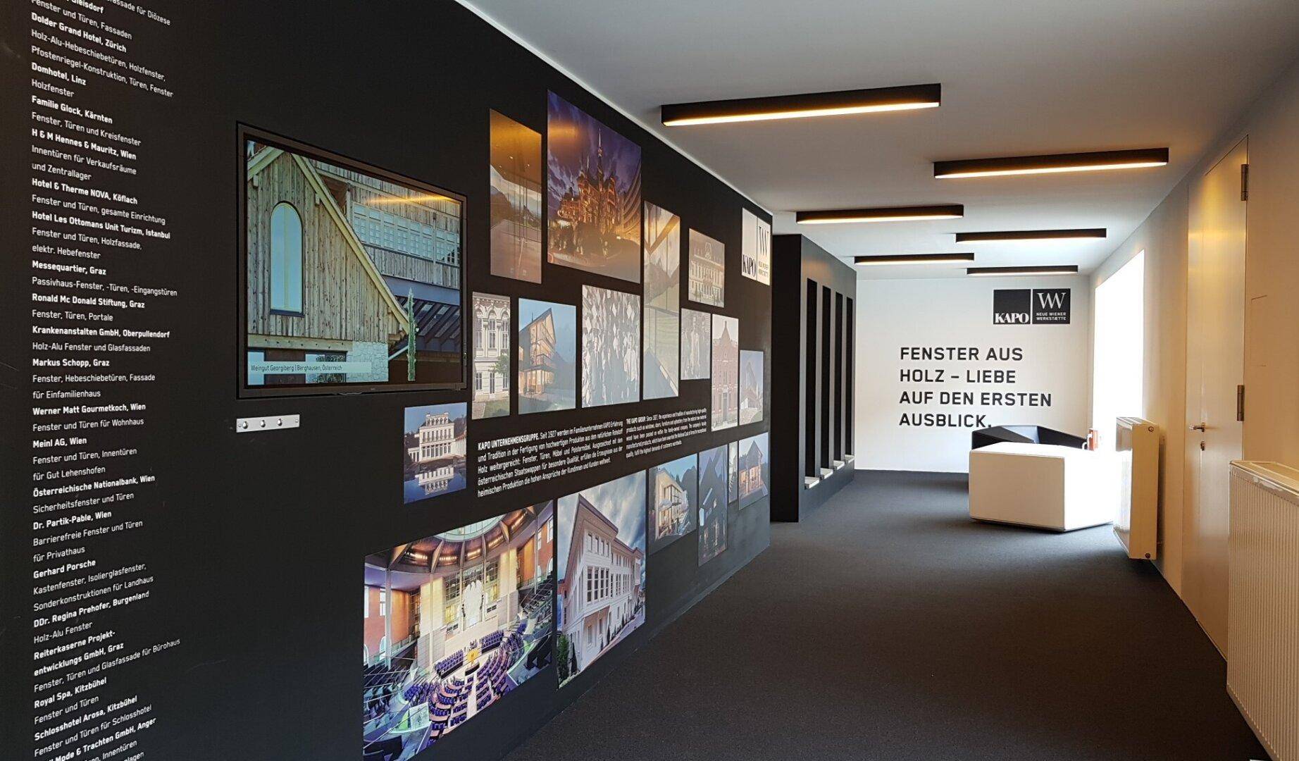 Langer, moderner Flur mit dunklem Teppichboden und informativen Ausstellungsstücken an den Wänden, beleuchtet von Deckenleuchten.