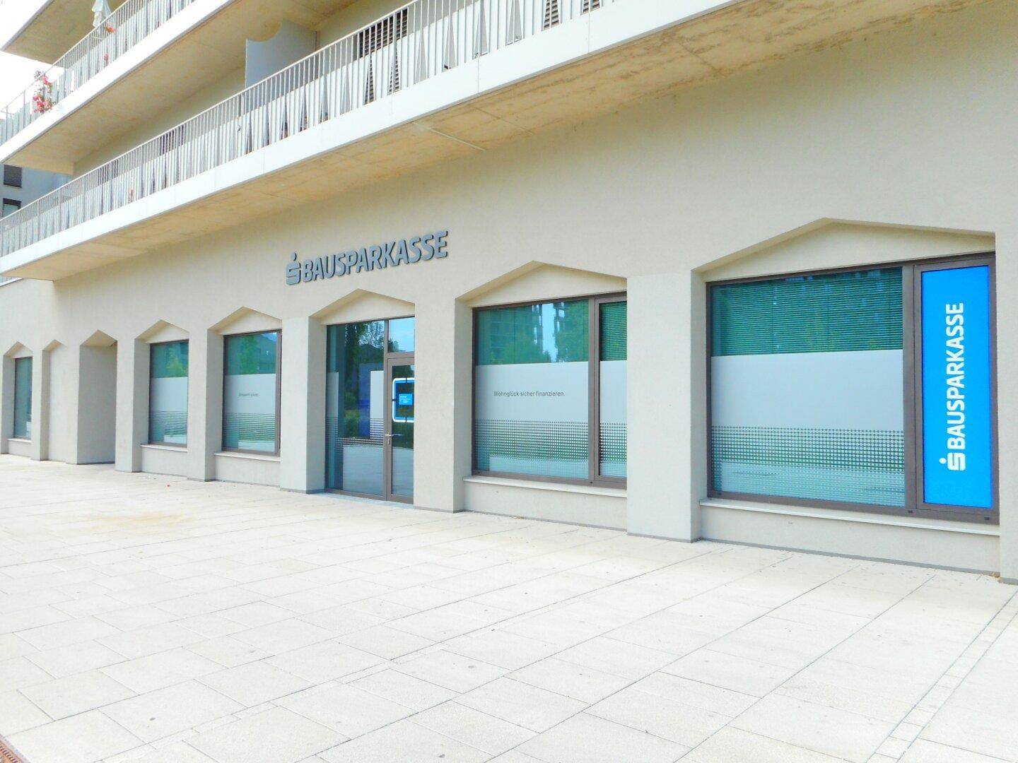 Geschäftsfassade der 'BAUSPARKASSE' mit großen Fenstern und einem Eingangsbereich in einem modernen Gebäude.