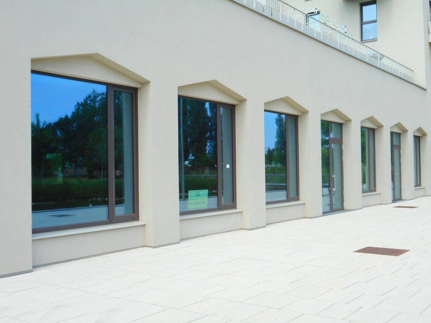 Detailansicht der modernen Gebäudefassade mit einer Reihe von großen Fenstern und einem hellen Gehweg davor.
