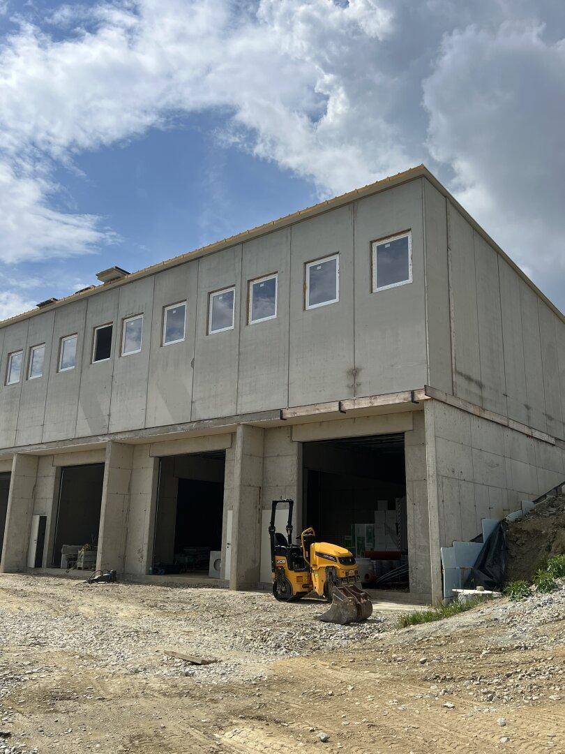 Neubau eines Gewerbegebäudes mit Betonfassade und Baumaschinen auf der Baustelle.