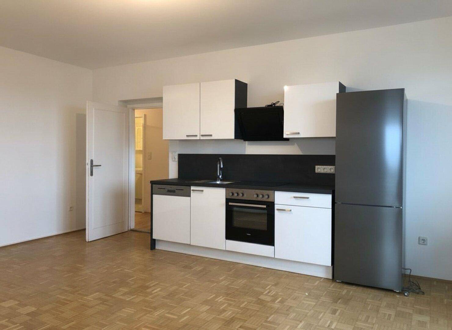 Funktionale Küchenzeile mit weißen Fronten und integrierten Geräten in einem Raum mit Fischgrätparkett.
