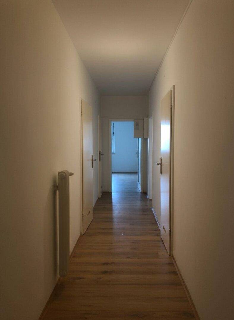 Langer, heller Flur mit Holzfußboden und weißen Wänden, der zu verschiedenen Zimmern führt.