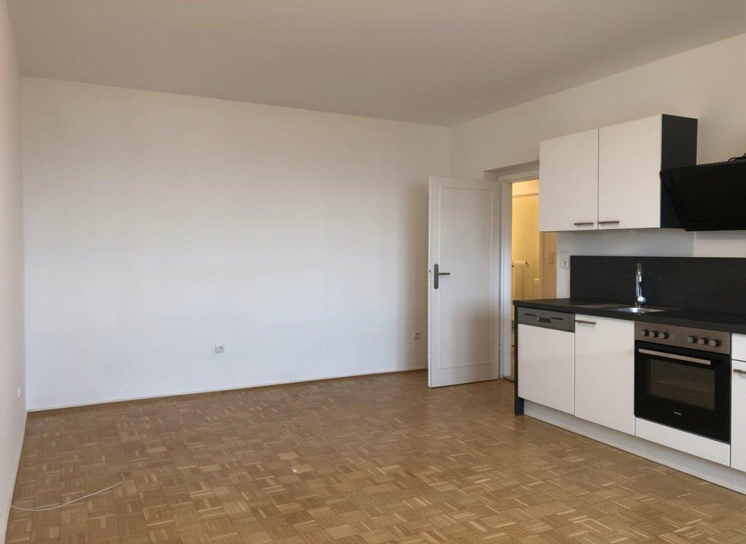 Heller Raum mit Parkettboden und einer kompakten Küchenzeile an der Wand, bereit zur individuellen Gestaltung.