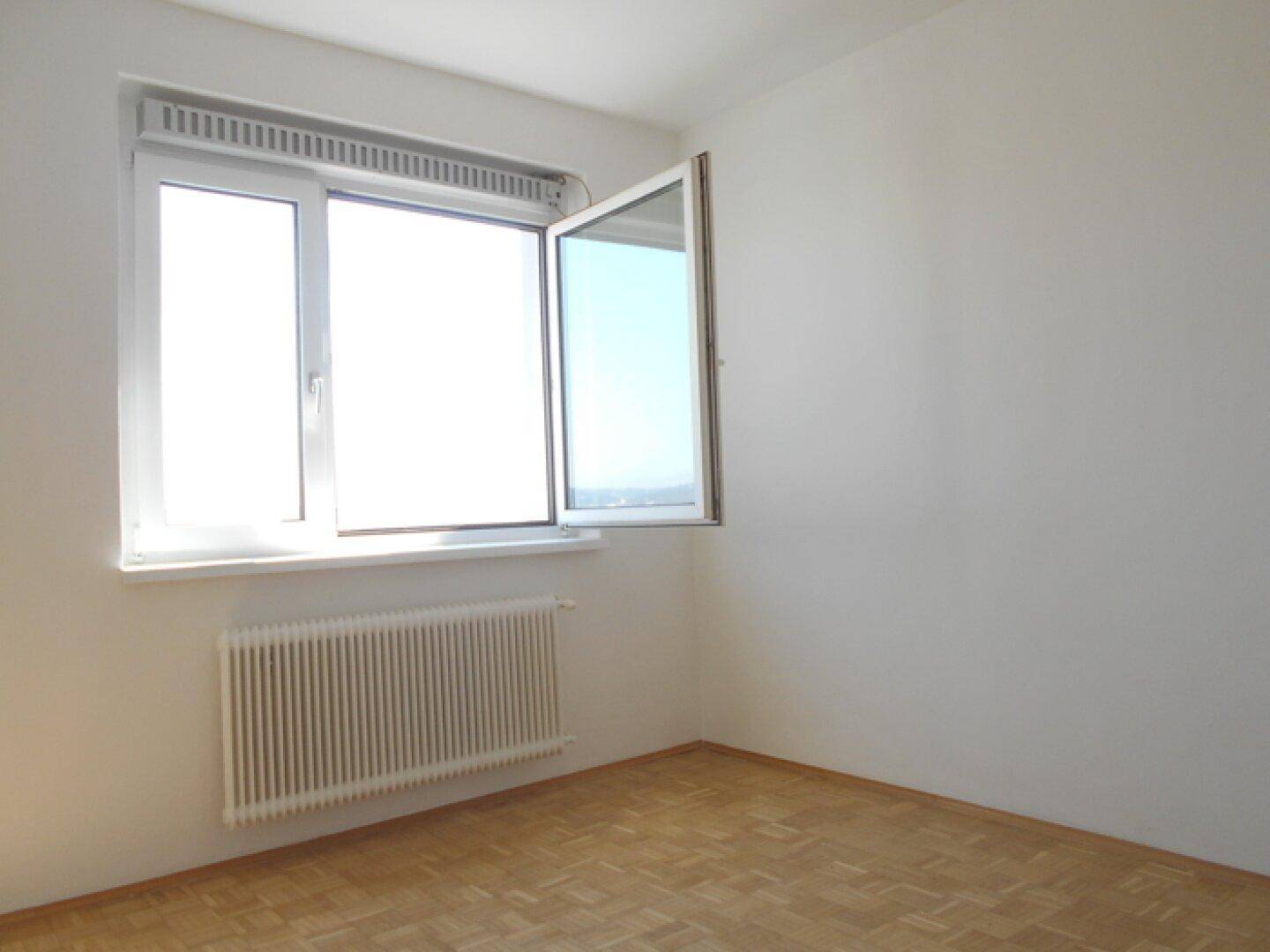 Helles Schlafzimmer mit Parkettboden, weiß gestrichenen Wänden und einem großen Fenster für viel Tageslicht.