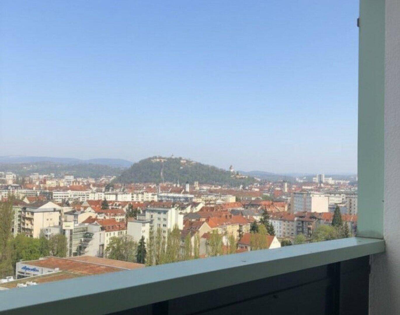 Panoramablick über die Stadt mit Gebäuden und grünen Hügeln im Hintergrund unter klarem blauem Himmel.