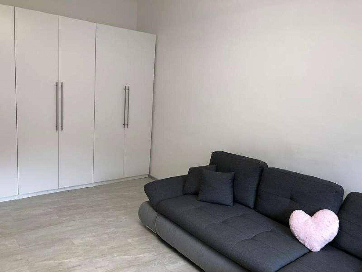 Wohnzimmer mit großem Ecksofa und integrierten weißen Kleiderschränken an der Wand.