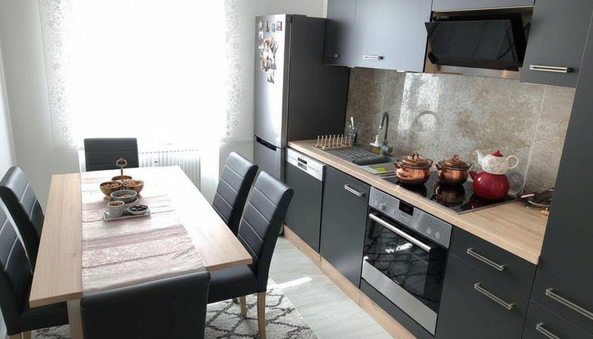 Moderne Küche mit dunklen Schränken, Holzarbeitsplatte und Essbereich am Fenster.