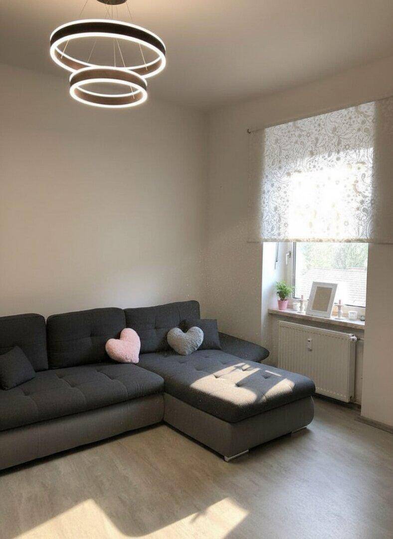 Gemütliches Wohnzimmer mit großem Ecksofa, modernem Deckenlicht und hellem Laminatboden.