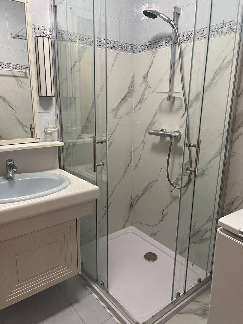 Helles Badezimmer mit moderner Duschkabine, Marmoroptik-Fliesen und einem einzelnen Waschbecken mit Unterschrank.