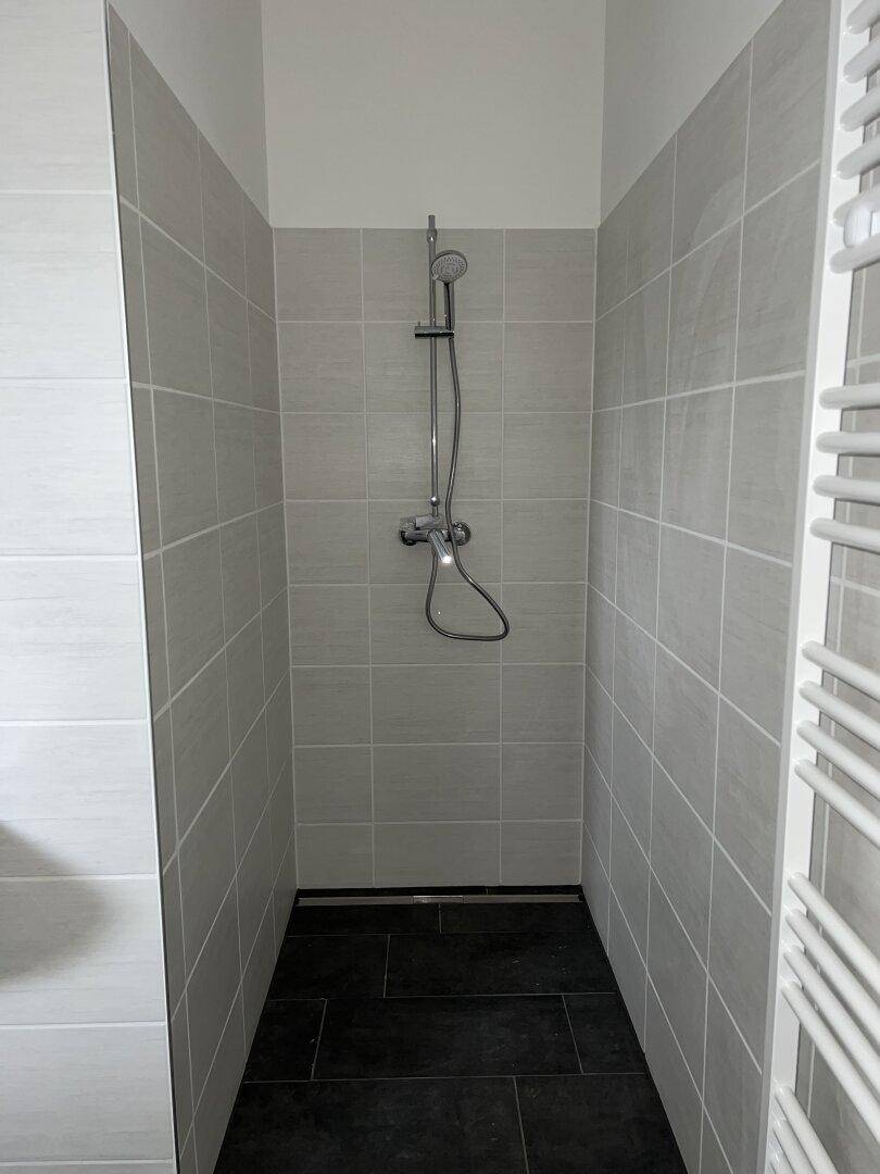 Moderne Duschkabine mit hellgrauen Wandfliesen und dunklem Boden sowie Handtuchheizkörper.