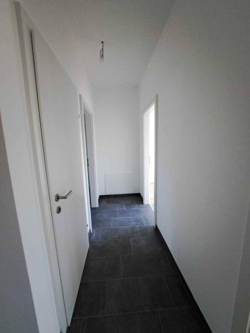 Heller Flur mit dunklen Fliesen und weißen Wänden, der zu weiteren Räumen führt.
