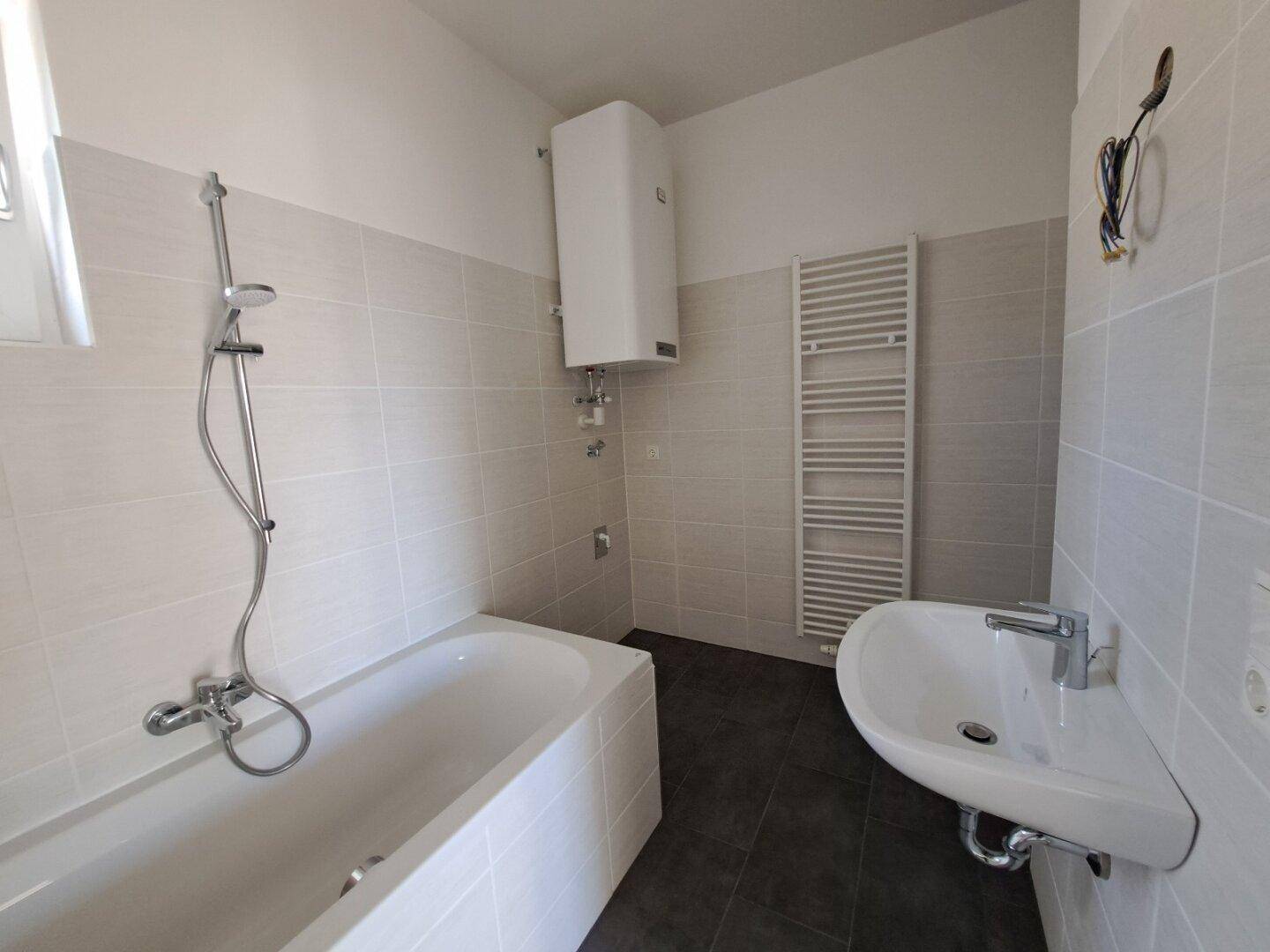 Badezimmer mit Badewanne, Waschbecken, Handtuchheizkörper und hellgrauen Wandfliesen.