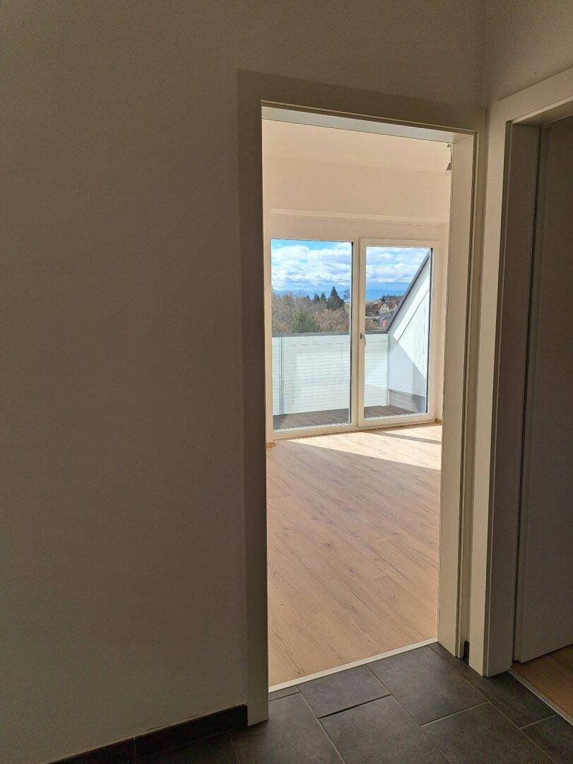 Blick durch eine Tür in einen hellen Raum mit Balkonzugang und weitem Ausblick.